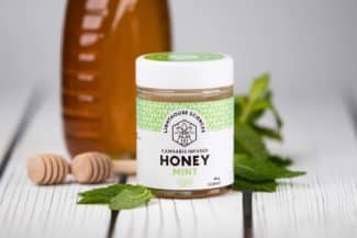 Lighthouse Sciences Cannabis Infused Mint Honey Jar on wood table surround by mint and Honey Bottle